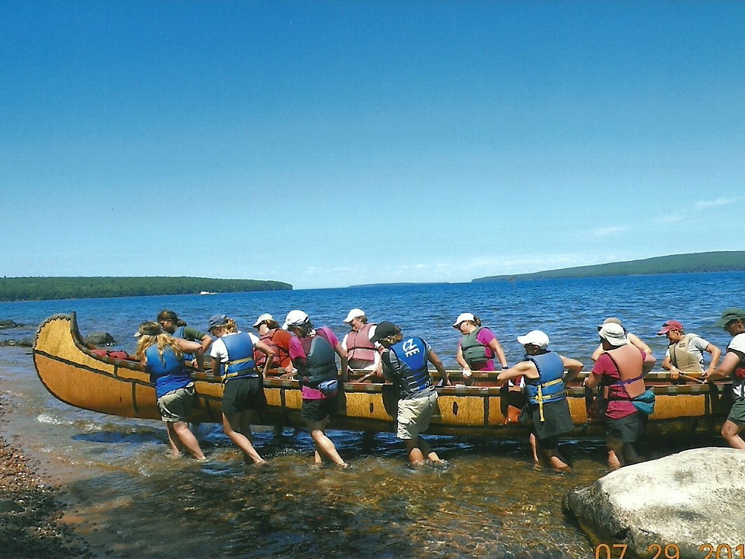 A team of women work together to pull a 35' Montreal Canoe onto shore in the Apostle Islands